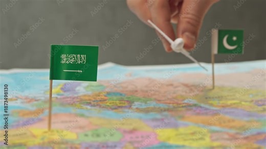 Toy airplane flying from Pakistan to Saudi Arabia above colorful world map, symbol Hajj routes, expatriate workers, regional airlines and intensive Gulf air traffic.