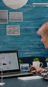 Vertical video: Middle aged senior older woman elearning online concept, watching business graphs, charts on laptop computer remote working, social distance learning, writing notes from home office.