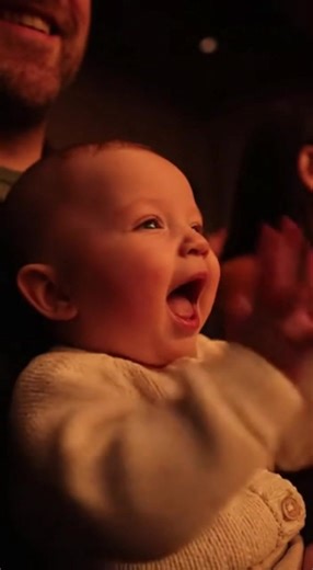 A baby hears applause at a show and enthusiastically joins in. When the clapping stops, the baby continues their joyful solo performance, clapping with pure delight. The parents watch with tender amusement as their little one creates their own encore. | Jarche