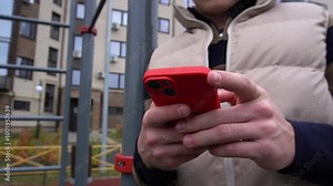 red smartphone in the hands of a teenager outside the building.