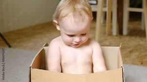 Baby in the Box. Pretty baby infant girl sitting inside a Cardboard box. Baby toddler in a carton box playing, smiling and hiding. Peekaboo. Game of hide and seek. International shipping worldwide.