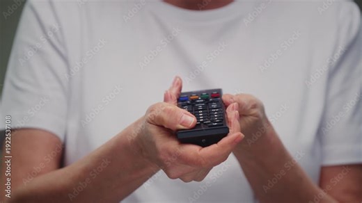 Remote control is in old hands. Old man or elderly woman turns on an old TV and holds the remote control in his palms. Retro viewer presses the buttons on the control panel. Switching channels. Key