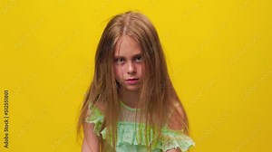 unhappy kid girl disheveled tousled and dirty hair and looking at camera on the yellow background, studio shot. children scalp problems, scratch hair