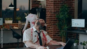 Scary dead walking zombie working on modern computer. Brain-eating spooky monster with bloody and deep wounds sitting at desk in office while trying to use laptop for reading documents.