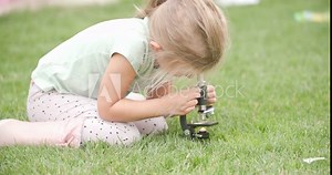 clever little blonde kid being curious, looking through microscope, researching and making science outdoor in backyard