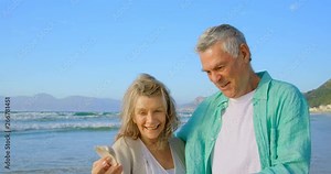 Front view of senior Caucasian couple holding a seashell on the beach 4k