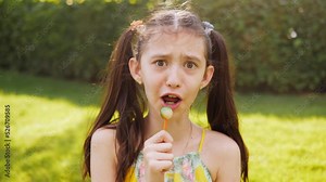 A preteen girl in the park licks a lollipop laughs and monkeys on camera