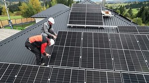 Technicians installing photovoltaic solar panels on roof of house. Drone view of men engineers in helmets building solar module system with help of hex key. Concept of alternative, renewable energy.