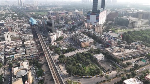 An expansive aerial of Noida Sector 18, where packed neighborhoods, metro infrastructure, and high-rises stretch into a hazy skyline—capturing urban density and pollution concerns.