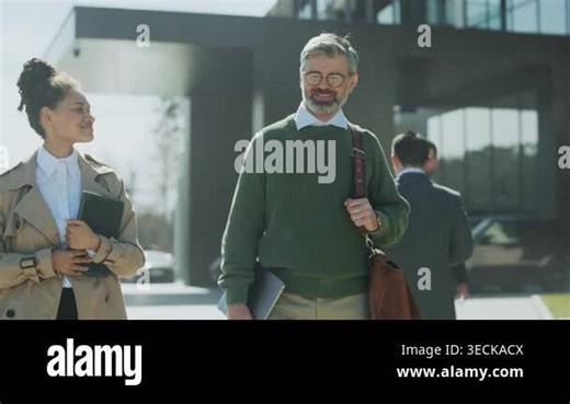 senior mentor and designer strolling outside modern campus, warm smiles and friendly eye contact, leather satchel Stock Video Footage - Alamy
