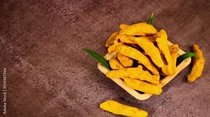 whole turmeric fingers or sticks in a bowl with green leaves on wooden background dark theme,dry turmeric curcuma or halkund rotation