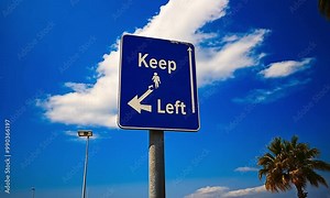 A blue road sign indicating to keep left with a pedestrian icon under a clear sky.