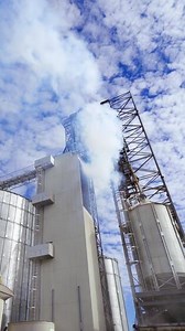 Modern factory for grain storage. Massive smoke from industrial plant. Large silver containers for drying grains. Pollution the environment. Vertical