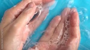 Woman washing hands with soap in blue water background. Soapsuds bubbles on palm. Cleanliness and body care concept.