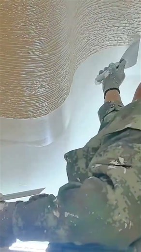 Skilled plasterer creating smooth textured ceiling curves with precision