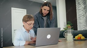 A senior Caucasian woman using a laptop with her adult daughter at home.