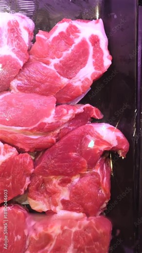 Fresh uncooked pork steaks and ribs cooling in a refrigerated display case at a supermarket butcher department. Close up view of raw meat selection ready for customers to purchase for cooking