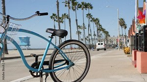 Blue bicycle, cruiser bike by ocean beach, pacific coast, Oceanside California USA. Summertime vacations, sea shore. Vintage cycle by beachfront house, waterfront cotteges, bungalow huts and palm tree