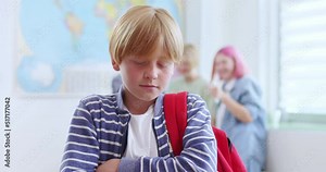 Sad bullied boy standing in classroom while three classmates behind him scoffing. Concept of discrimination and negative communication in society.