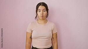 Crazy fun, young, beautiful hispanic woman making comical fish face, squinting eyes. strikes a silly pose over pink isolated background, channeling mad joy through a playful gesture