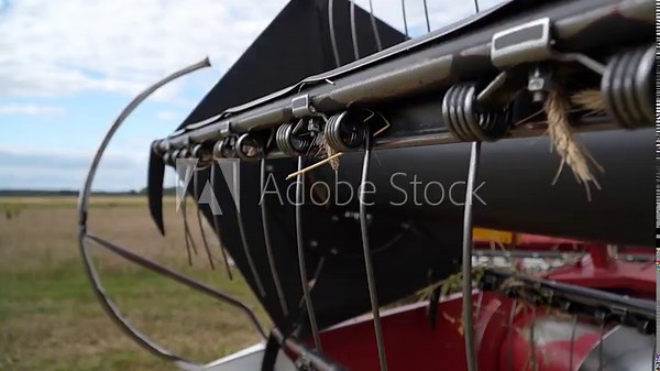 Close-up of combine harvester header detail with metal mechanism and wires. Head of combine harvester machine with reel and cutting gear raised working in wheat field in summer cutting barley and whea