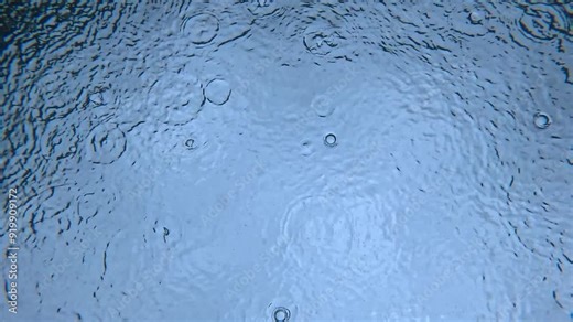 An underwater view capturing raindrops hitting the water’s surface, creating concentric circles above. The unique perspective showcases the interaction between rain and water. Stock Video
