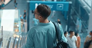 Man in blue shirt descends on escalator into subway showcasing urban travel. His descent on escalator, blend of style and city life Each step down on escalator marks journey through bustling city.
