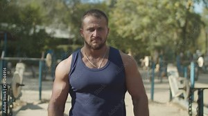 Portrait of concentrated muscular built strong bodybuilder walking through rows of exercise machines, preparing for strength training during outdoor workout, expressing determination and confidence.