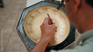 Master engraves patterns on a metal plate. Close-up, handmade, tinsmith, working with hammer during hand stamping or engraving decoration pattern on metal tray. Copper master, hands detail of