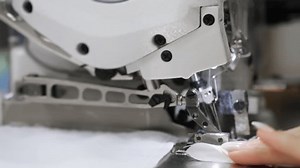 Factory for the production of clothing. Close-up of a sewing machine at work. A girl sews clothes on a sewing machine.