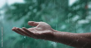 Rain drops falling on man's hand during the rainy day on green nature background, cinematic shot. Male hand catching rain drops in nature. Male hand under falling rain waters, slow motion, close up