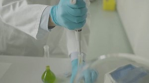 Scientist in gloves using pipette with green solution in lab setting close-up