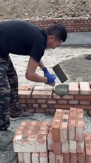 Laying red bricks on cement mortar to build a wall with skilled hands