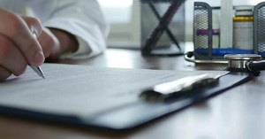 Doctor Writes on Form with Pen in Office