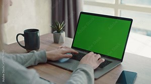 Woman typing and surfing internet on green screened laptop. Female hands typing on a green screen laptop on the desk with coffe and smtphone near the window