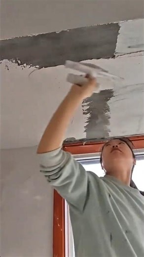 applying smooth white plaster on a gray ceiling surface using a manual white plastic trowel tool
