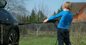 Kid Uses Pressure Car Washer to Clean Auto in Backyard. Child Helps Washing Vehicle. 4K Slow motion 60 fps 10-bit