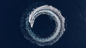 Aerial top view of a motor RIB boat forming a circle of waves and bubbles with its engine over the blue sea