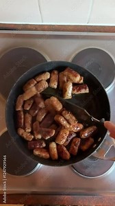 overhead view of person cooking food, stirring cevapi in frypan on electric cooktop