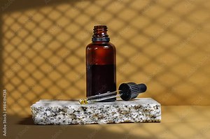 Blank amber glass essential oil bottle with pipette on brown background with twist mesh window shadow. Skin care concept with natural cosmetics