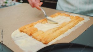 Women's hands spread cream on puff pastry sticks. Delicious simple puff pastry cake recipe. Close-up of the table. Cooking in the kitchen