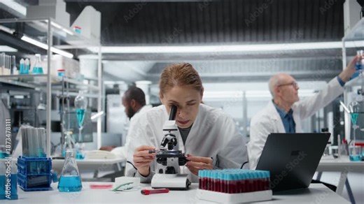 Female microscopist examining microscope glass slide in laboratory to view cells. Research facility employee checks sample slide, doing imaging process using optical device, camera A