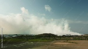 A fire at a large city dump, a cloud of toxic smoke, rises into the sky. A fire helicopter extinguishes a fire using water, the work of firefighters. Environmental pollution, ecological disaster.