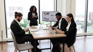 Business team counting money at table during meeting in modern office with large windows. Group of professionals in formal attire managing finances and discussing charts.