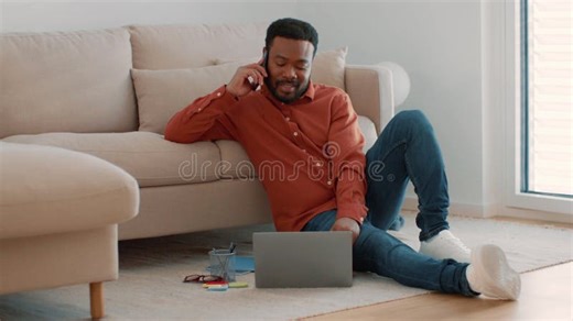 Man with Dark Skin Talking on Phone while Using Laptop at Home during Daytime Stock Video - Video of furniture, comfortable: 450418967