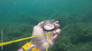 First-person view of a male hand holding a plastic magnetic compass rotates from the side and seeks the correct direction underwater.