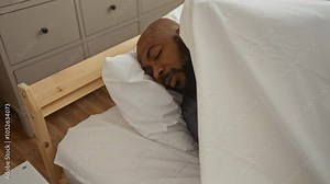 Man sleeping in bed at home bedroom with white sheets, peaceful and relaxed, showcasing a comfortable interior space.