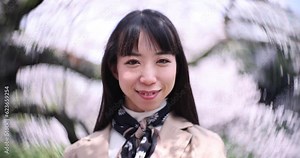 A 2x slow motion of swirly portrait by Japanese woman behind cherry blossom handheld
