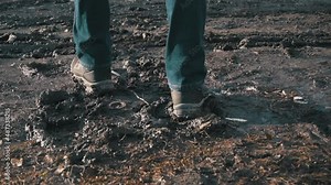 Man in boots walks through the mud, splashing from a puddle in slowmo. A guy in dirty shoes walks down the street. Rainy weather, slush. Close-up of a man's legs walking in a swampy area.