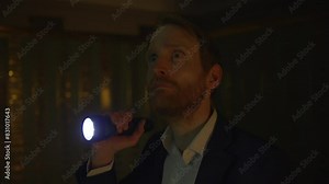 Man in suit, holding a flashlight in dimly lit room, creating mysterious and dramatic atmosphere